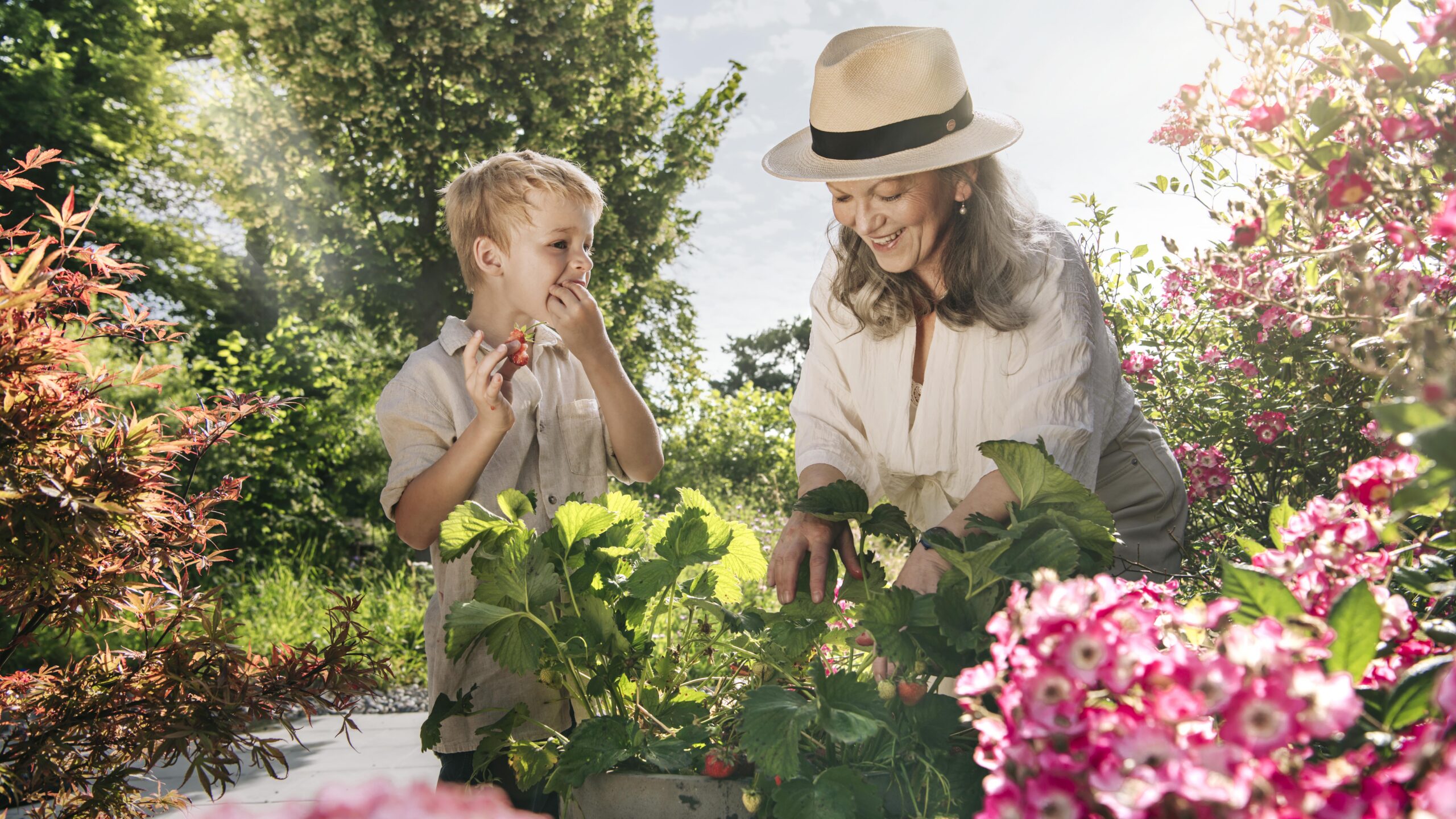 Zwei Frauen zwischen blühenden Sträuchern im Garten – B+G Schweiz Key Visual