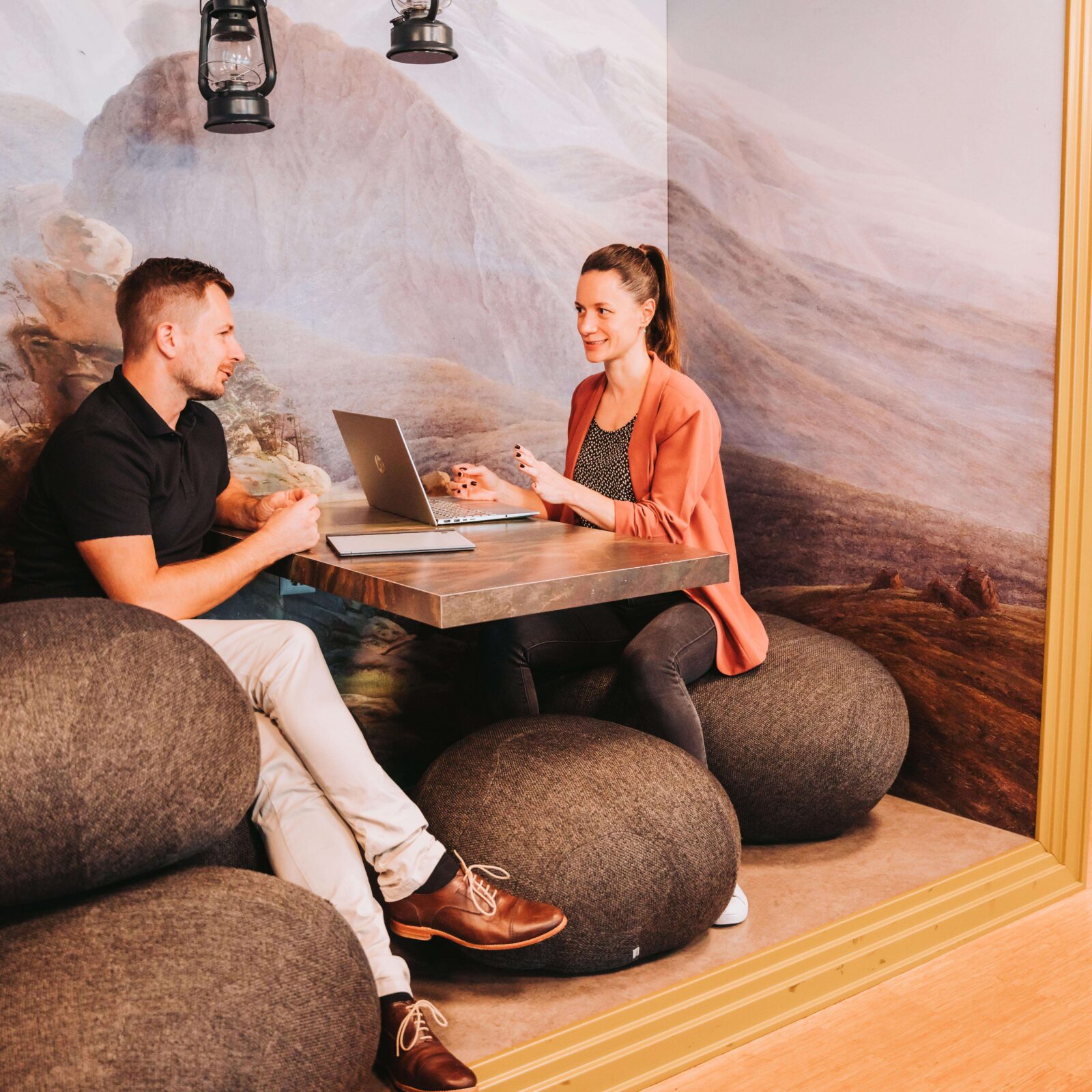 Zwei Personen im Gespräch in einer gemütlichen Lounge-Nische mit Laptop